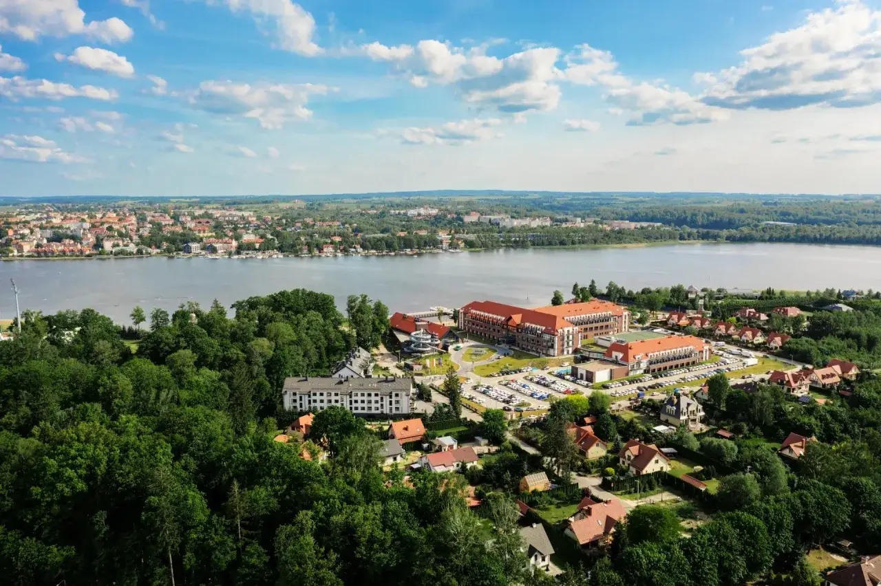 Hotel Lake Hill Mazury Resort & Spa z lotu ptaka, otoczony zielenią, z widokiem na jezioro i miasto.