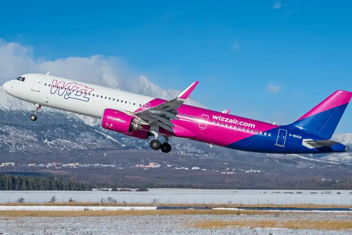 Samolot Wizz Air startuje na tle gór. Wizz Air to tania linia lotnicza, która oferuje loty po Europie.