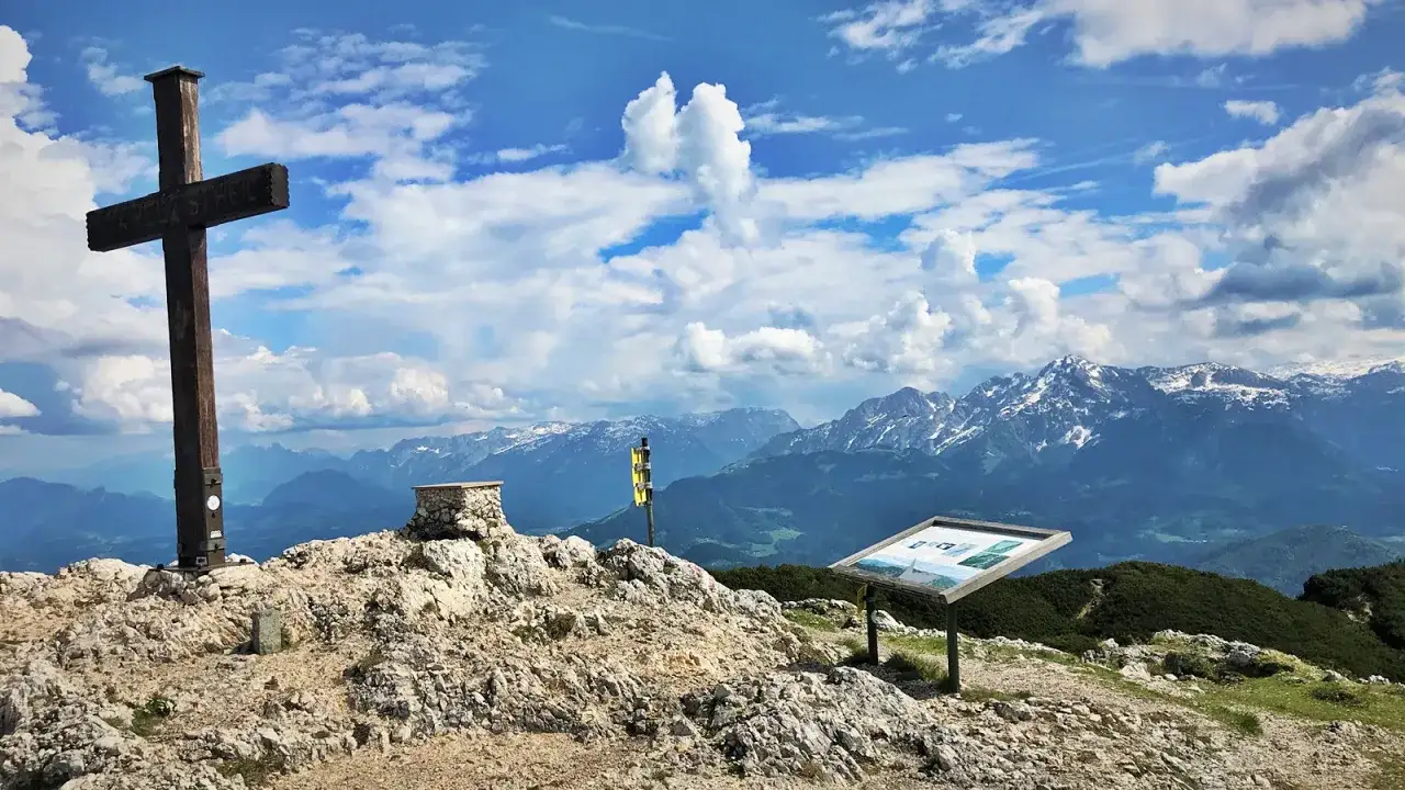 Holzkreuz auf felsigem Gipfel mit Panoramablick auf die schneebedeckten Alpen. Der Salzburger Hochthron ist ein majestätischer Anblick.