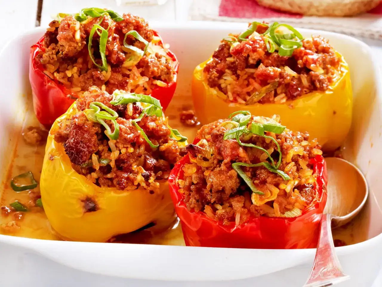 Gefüllte Paprika mit Hackfleisch und Reis, garniert mit Frühlingszwiebeln, in einer Auflaufform.