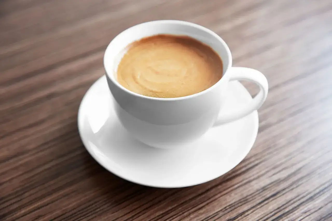 Tazza di caffè con schiuma cremosa su piattino bianco, perfetta per gustare la differenza tra caffè e ginseng.