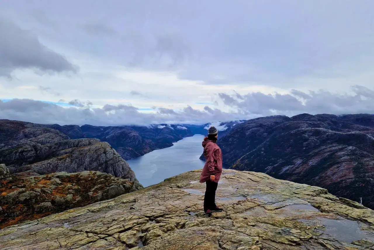 Widok na fiord z punktu widokowego. Osoba w kurtce podziwia krajobraz. To jedno z miejsc, kt&oacute;re warto zobaczyć w okolicach Stavanger.