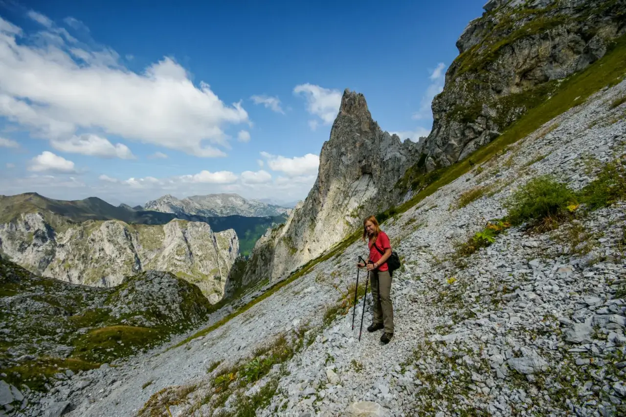 Kobieta z kijami trekkingowymi na skalistym zboczu, podziwiająca majestatyczne góry przeklęte.