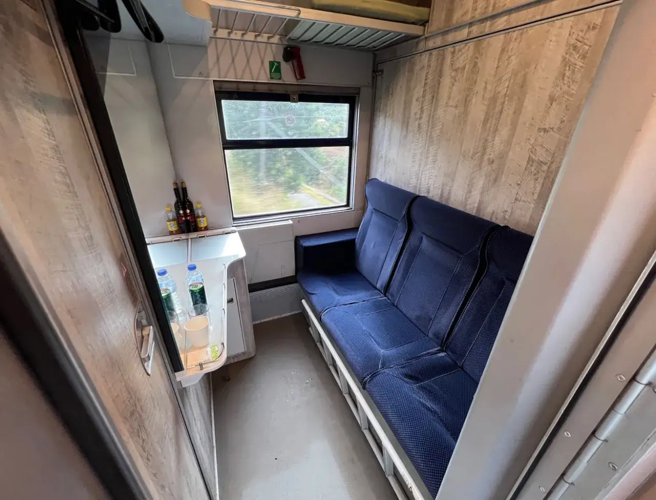 Gemütliche Kabine im Nachtzug Italien mit blauen Sitzen, Minibar und Blick ins Grüne.