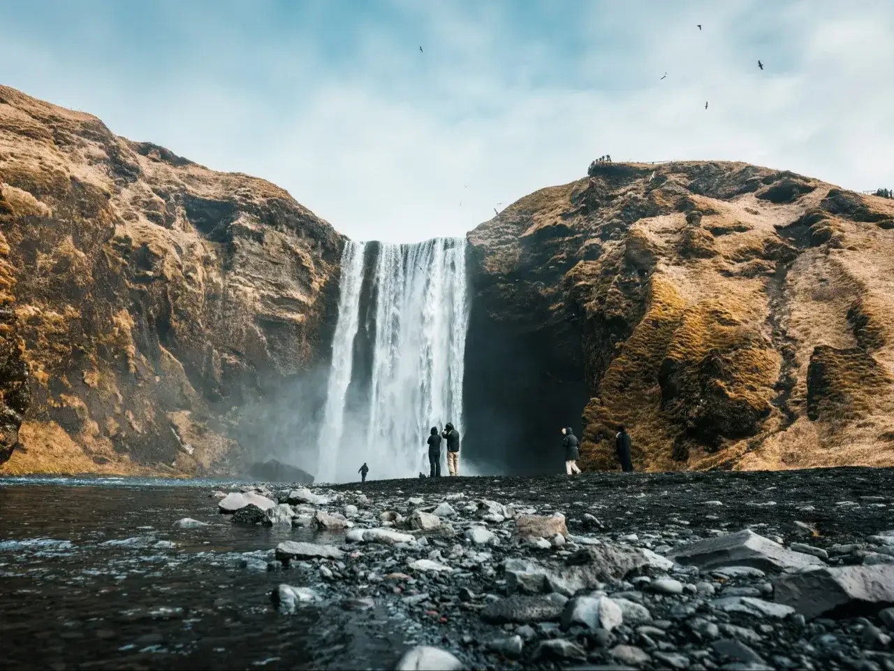 Wodospad Skógafoss na Islandii. Turyści podziwiają potęgę natury. Zastanawiasz się, ile trwa lot na Islandię?