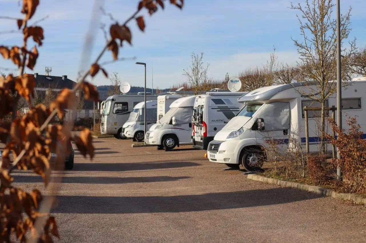 Une rangée de camping-cars blancs stationnés sur un parking. Un guide aire camping car serait utile pour trouver le meilleur spot.