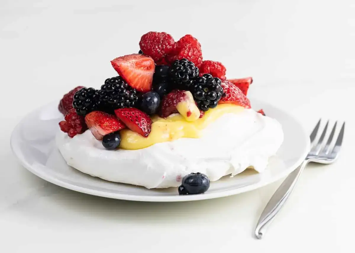 En fluffig pavlova med f&auml;rska b&auml;r och kr&auml;mig lemoncurd, redo att avnjutas med en gaffel.