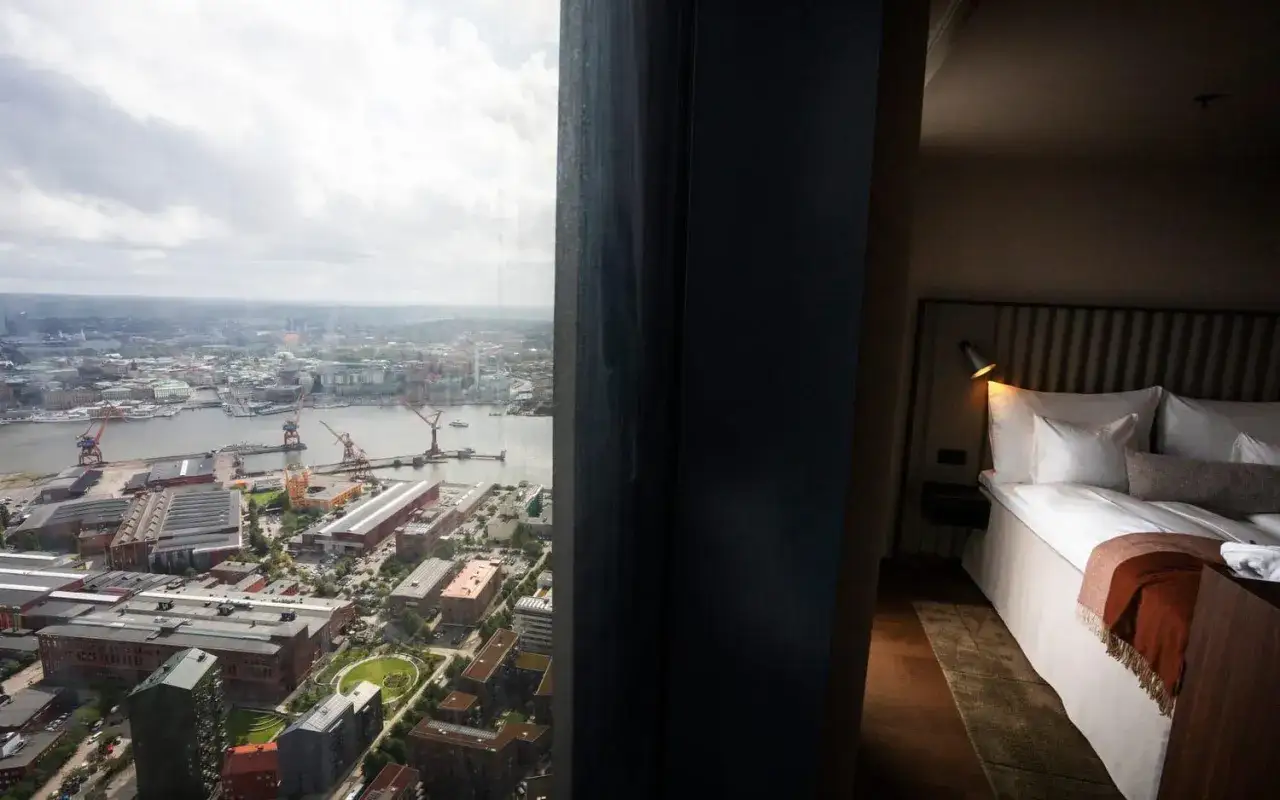 Vy från ett rum på Karlatornet hotell över Göteborgs hamn. En bekväm säng med vita lakan och en orange pläd.