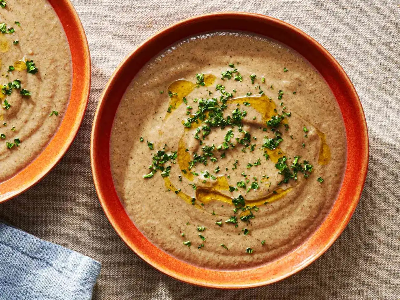 Zwei Teller cremiger **Pilzsuppe**, garniert mit Olivenöl und Petersilie, warten auf Genuss.