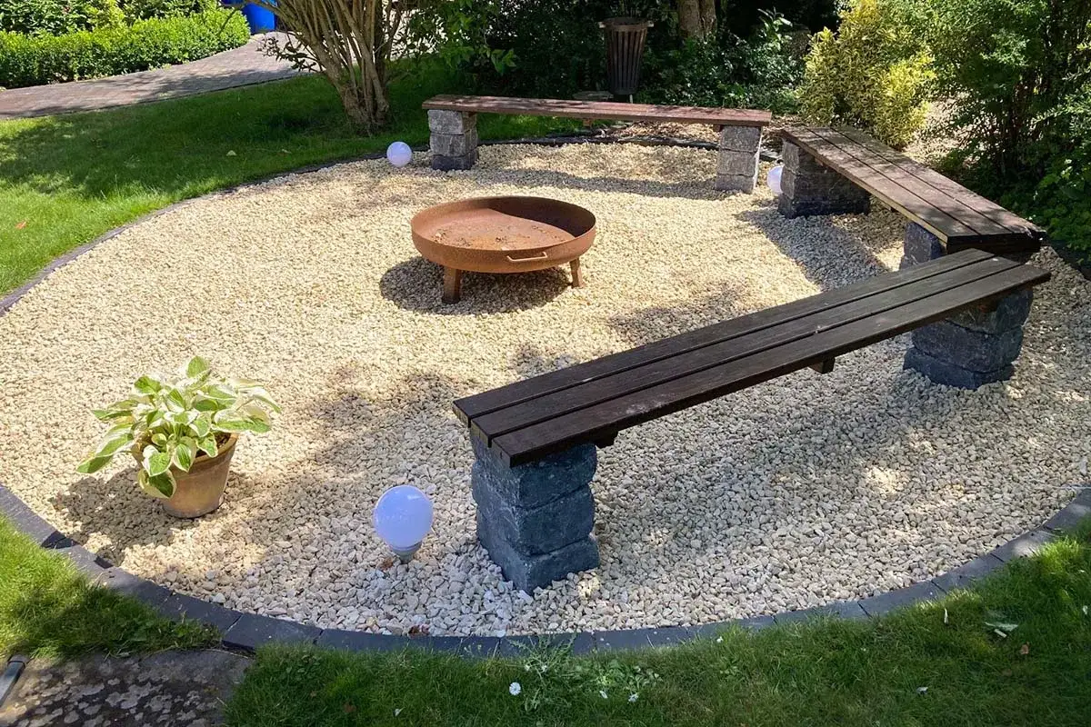 Gemütliche Feuerstelle mit Steinbänken und Kiesboden – eine tolle Idee, um eine tote Ecke im Garten gestalten.