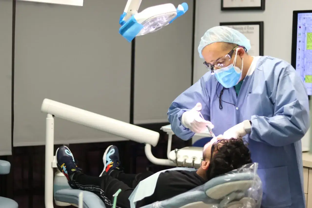 Dentista con equipo de protección realiza procedimiento para sacar muelas a paciente recostado en sillón dental.