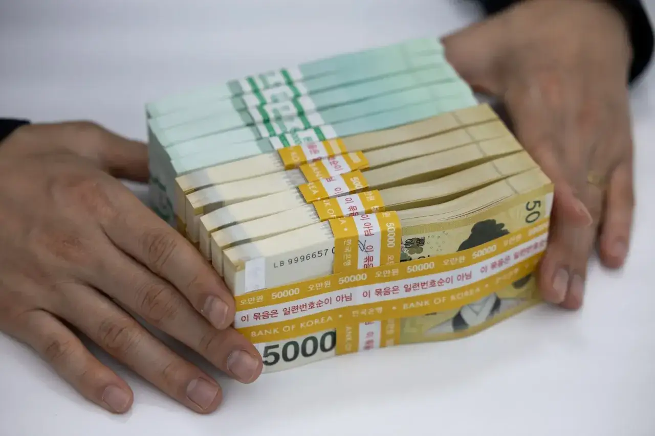 Dłonie trzymają stos banknotów. To waluta Korei Południowej, w tym banknoty o nominale 50 000 wonów.