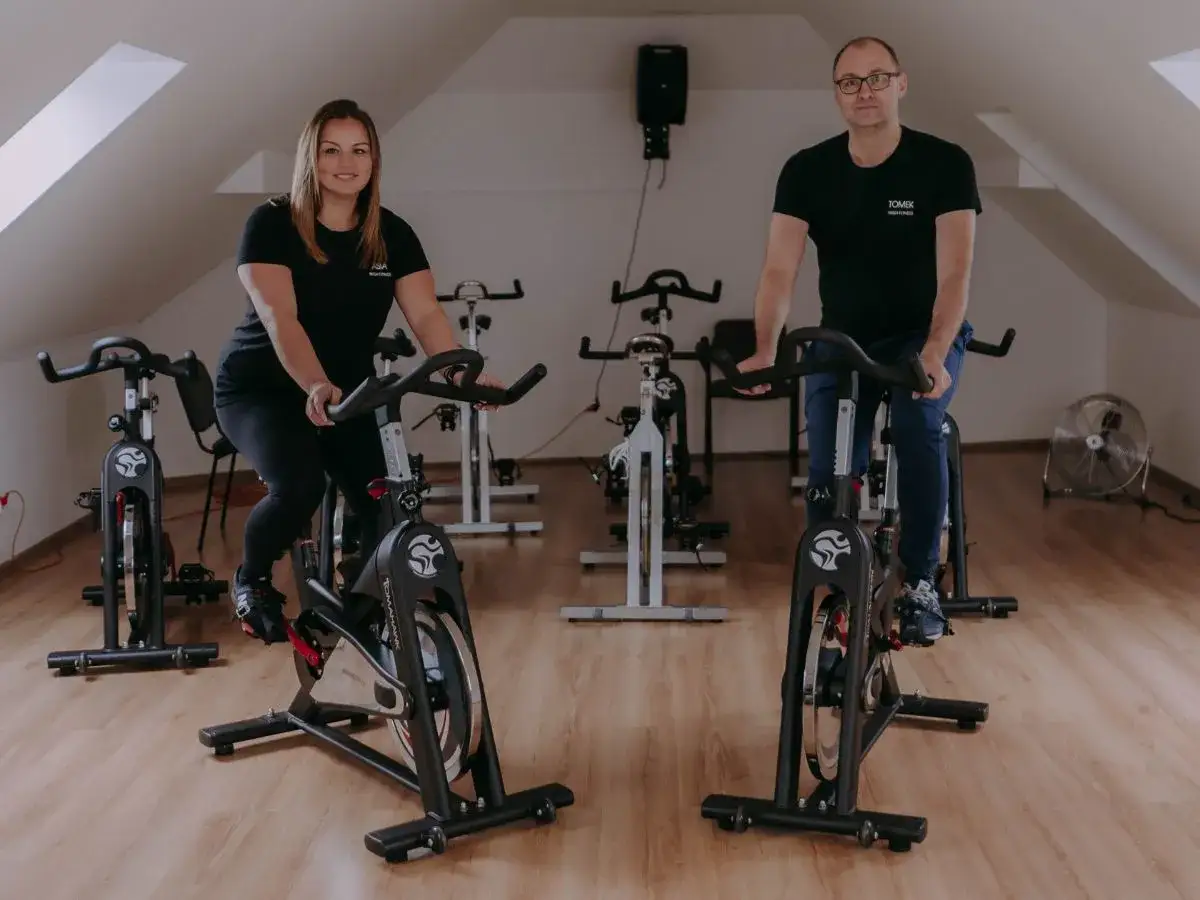Para, która wyjaśnia, indoor cycling co to jest, ćwiczy na rowerach stacjonarnych w sali treningowej.