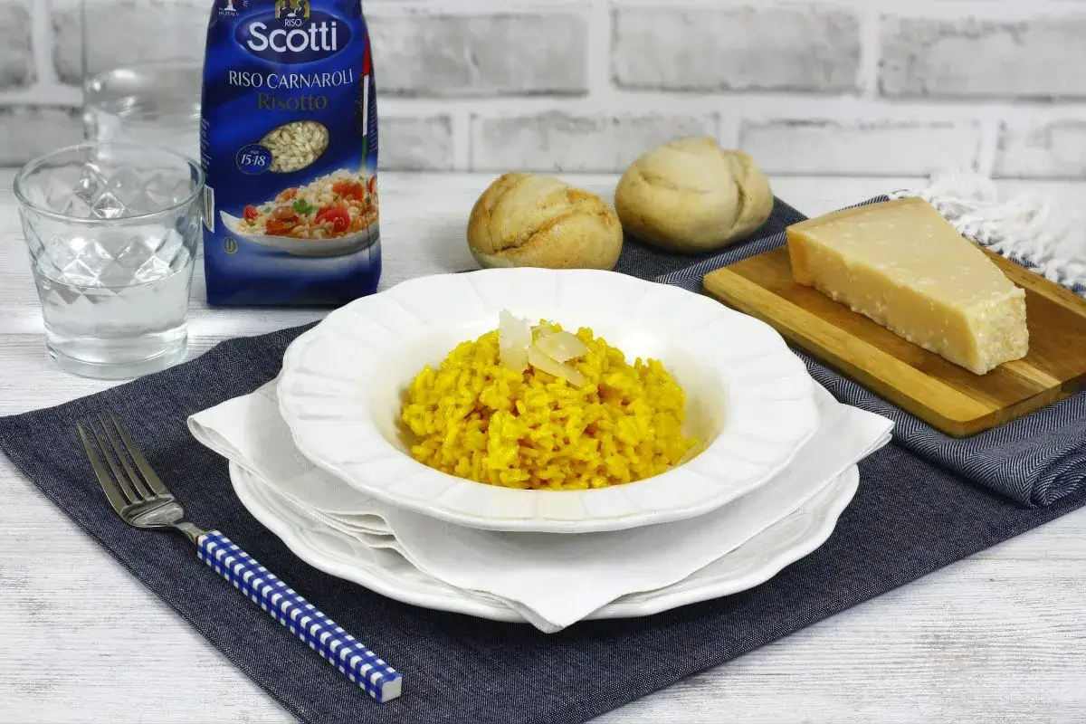 Un plato de risotto cremoso, con un trozo de queso Parmesano y panecillos. La bolsa de arroz Scotti indica de donde es el risotto: Italia.