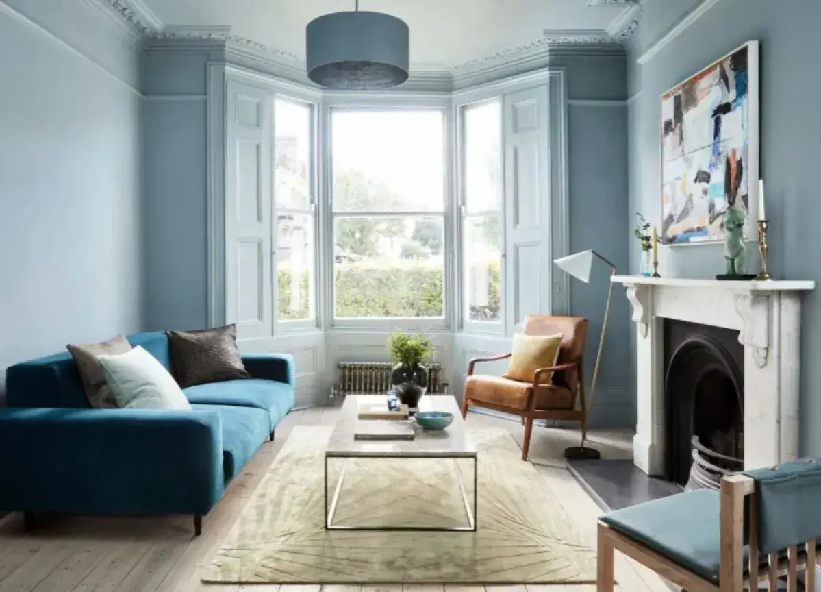Ein Wohnzimmer in sanften blau nuancen mit einem türkisfarbenen Sofa, Ledersessel und einem Kamin.