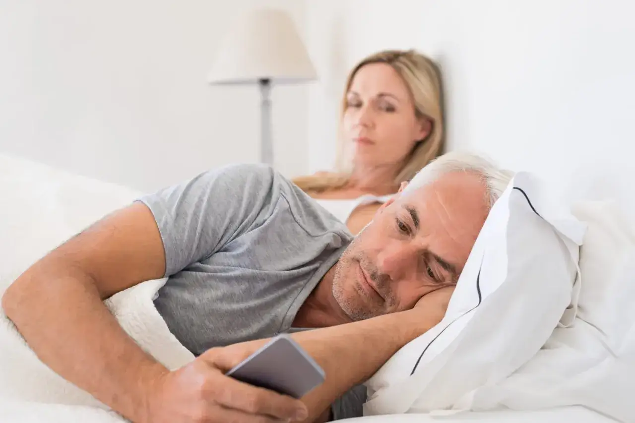 Un homme regarde son téléphone, l'air pensif, tandis que sa femme le regarde d'un air soupçonneux. Des signes d'un homme amoureux de sa maîtresse ?