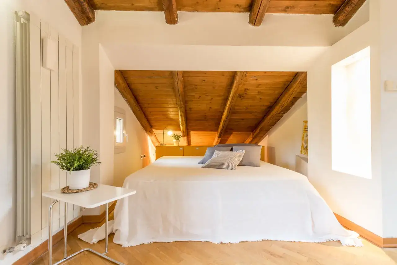 Accogliente camera da letto in mansarda con travi a vista in legno. Idee per un nido confortevole e luminoso.