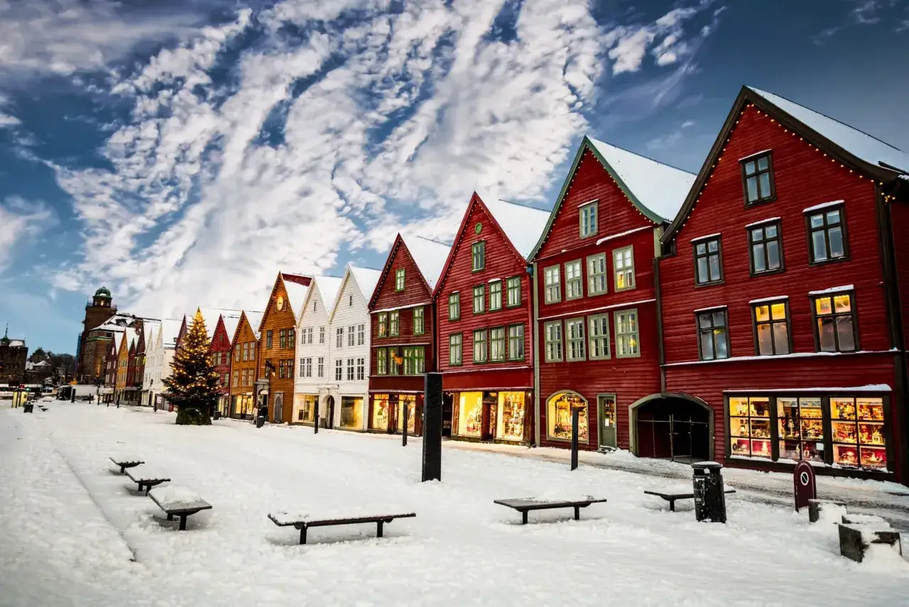Kolorowe domki Bryggen w Bergen zimą, pokryte śniegiem, z choinką i świątecznymi lampkami.