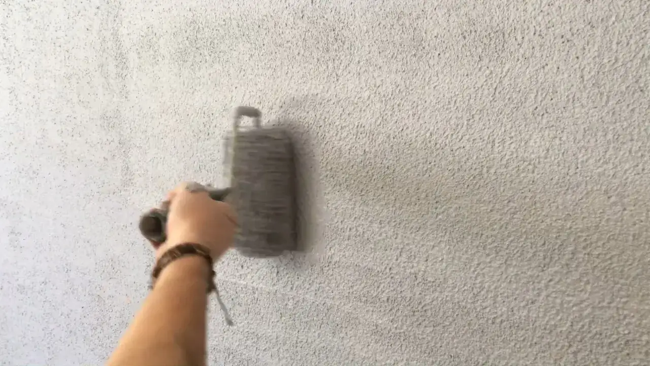 Main d'une personne appliquant un crépi au rouleau sur un mur texturé.