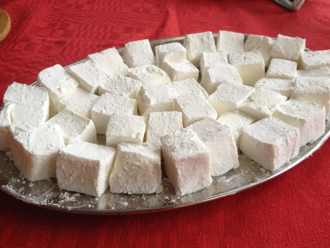 En silverbricka fylld med fluffiga, hemmagjorda marshmallows, pudrade med socker, ligger p&aring; en r&ouml;d duk.
