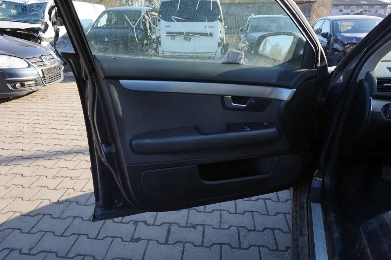 Wnętrze Audi B7, widok na otwarte drzwi i zniszczone samochody na placu złomowiska.