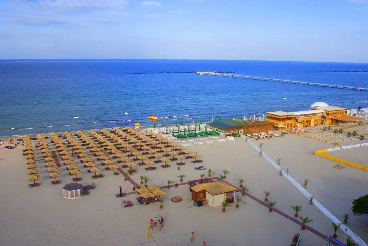 Słoneczne plaże w Konstancy, rzędy parasoli, budynki plażowe i długie molo na Morzu Czarnym.