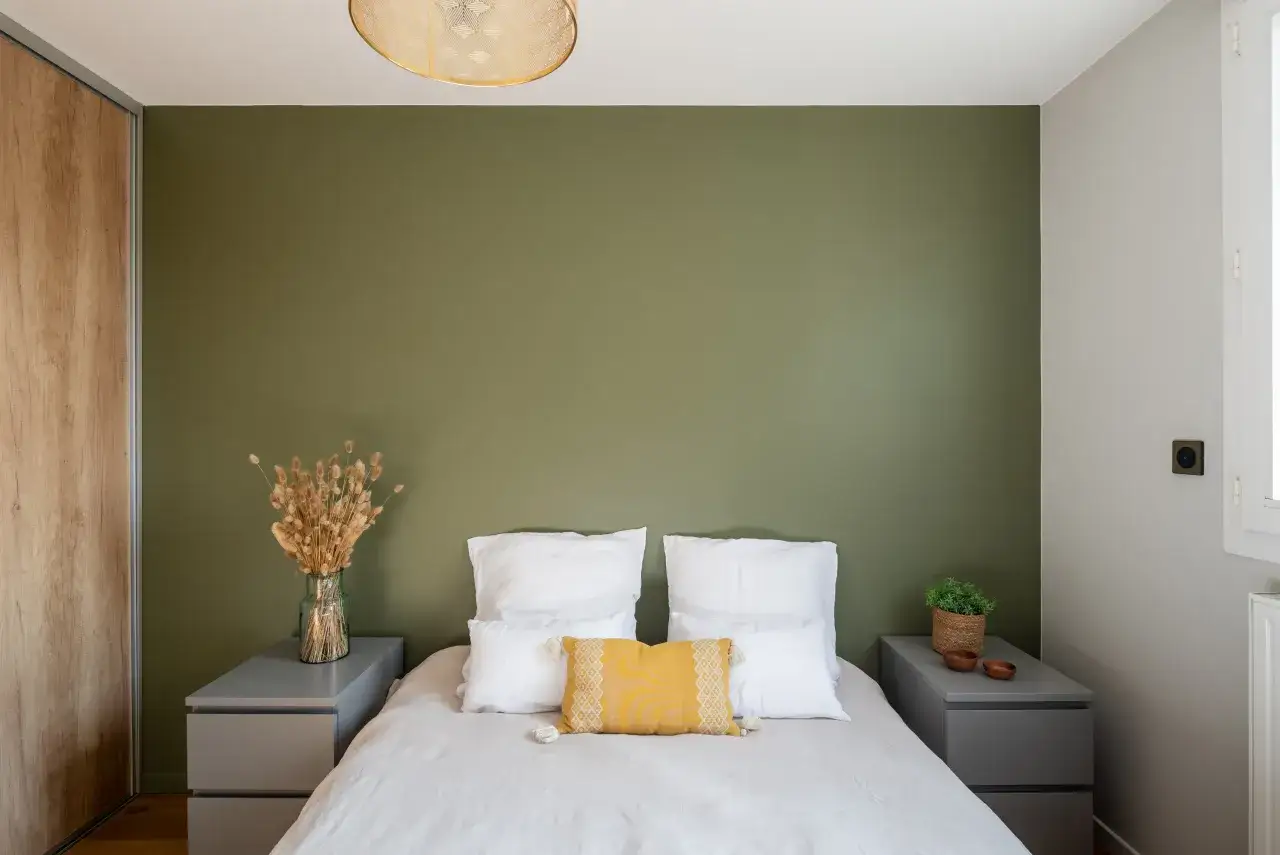 Chambre apaisante avec mur vert forêt, lit blanc et coussin jaune. Des nuances de vert apportent une touche naturelle.
