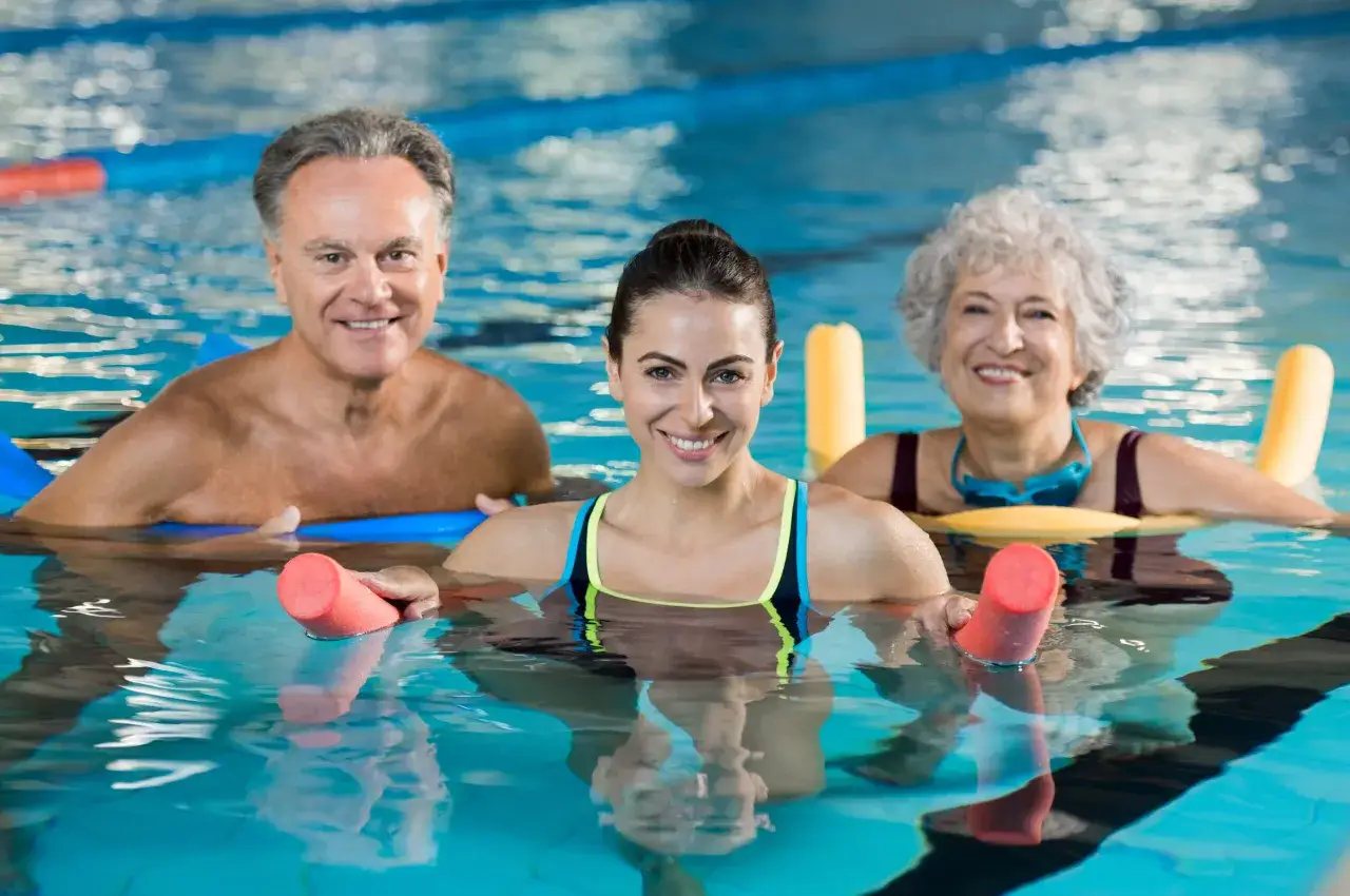 Drei l&auml;chelnde Menschen genie&szlig;en Wassergymnastik. Schwimmen bei Arthrose ist eine Wohltat f&uuml;r Gelenke und Wohlbefinden.