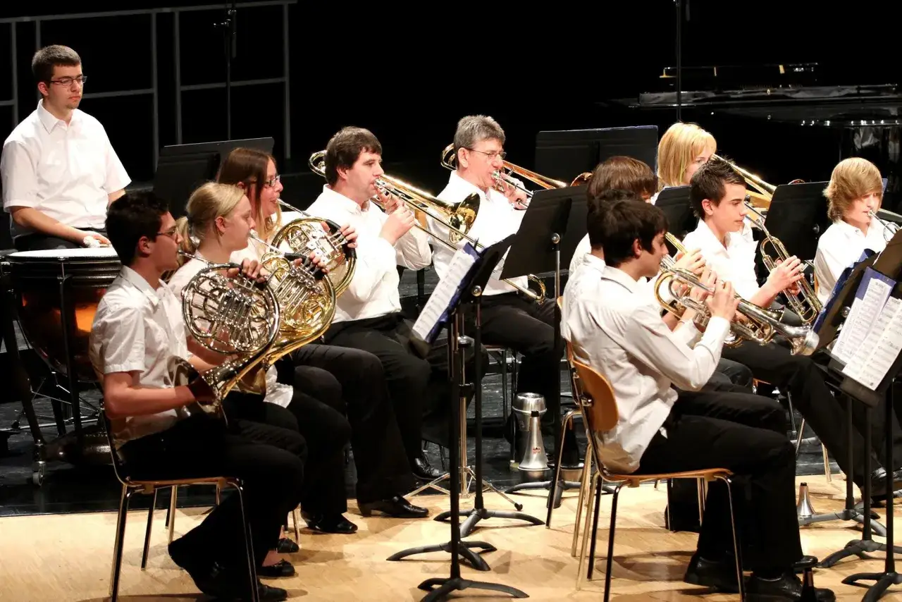 Un orchestre joue, plusieurs musiciens tiennent un gros instrument &agrave; vent, comme des cors d'harmonie et des trombones.