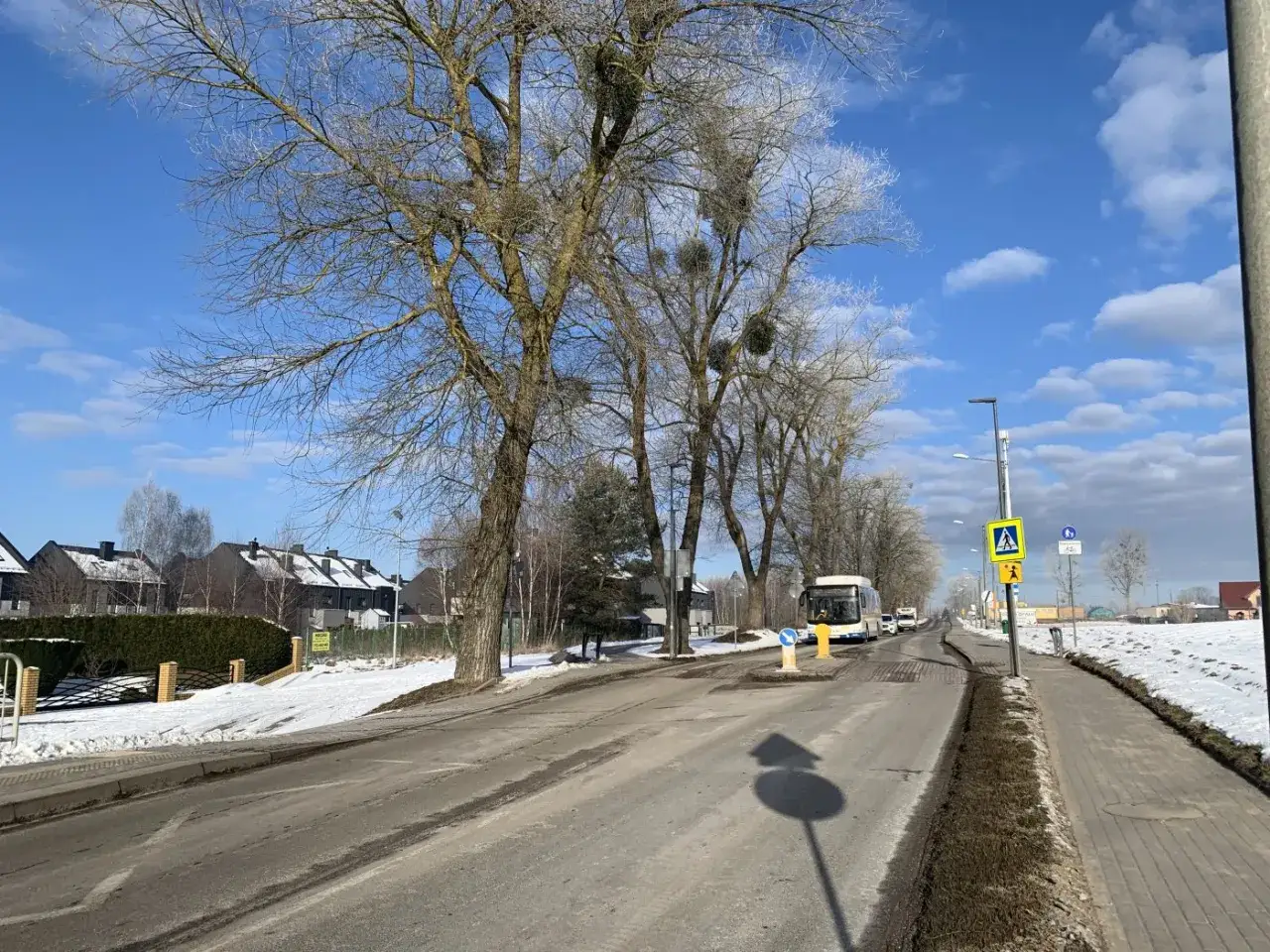 Zima na wsi, droga, drzewa, domy i autobus. Zastanawiasz się, jak napisać wniosek o budowę chodnika?