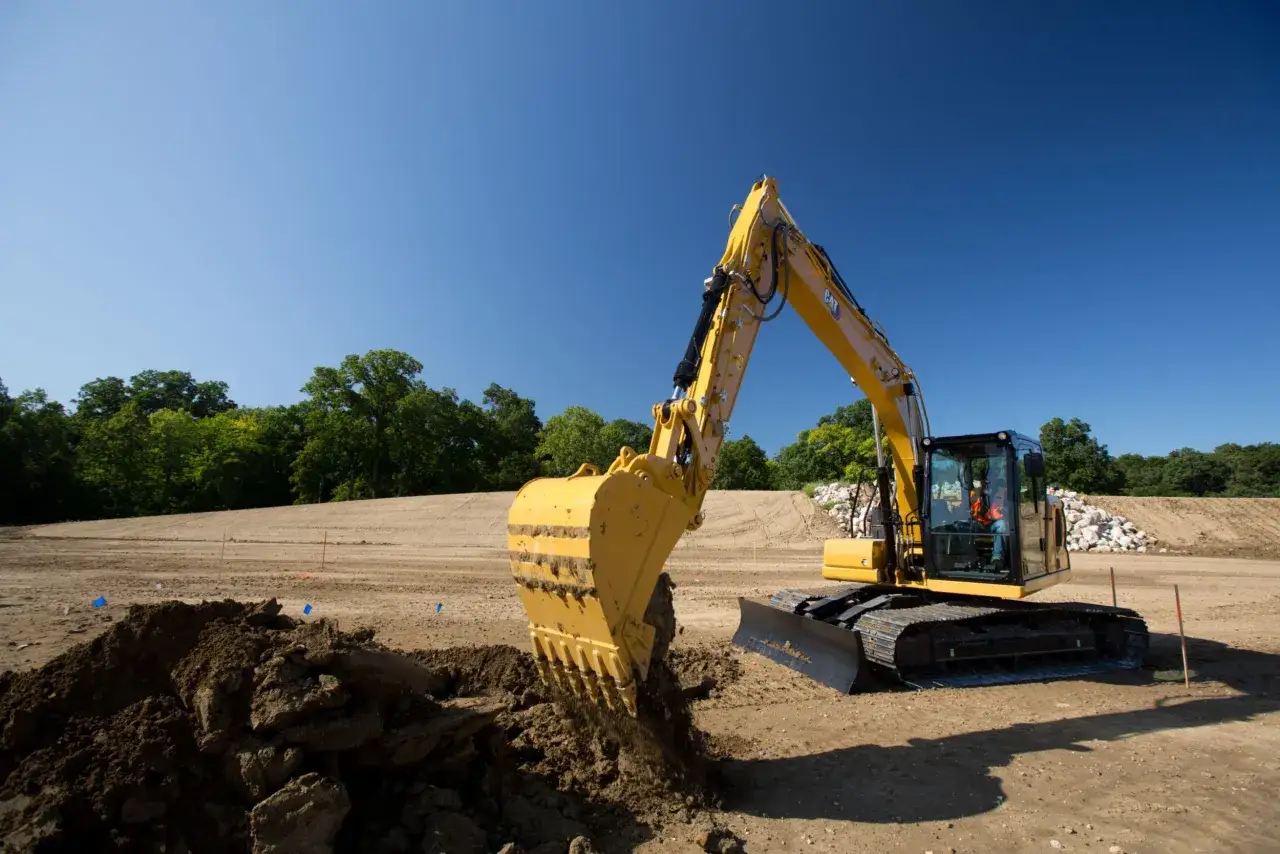 Koparka Cat 313 pracuje na budowie, nabierając ziemię. Dane techniczne tej maszyny pozwalają na efektywne prace ziemne.