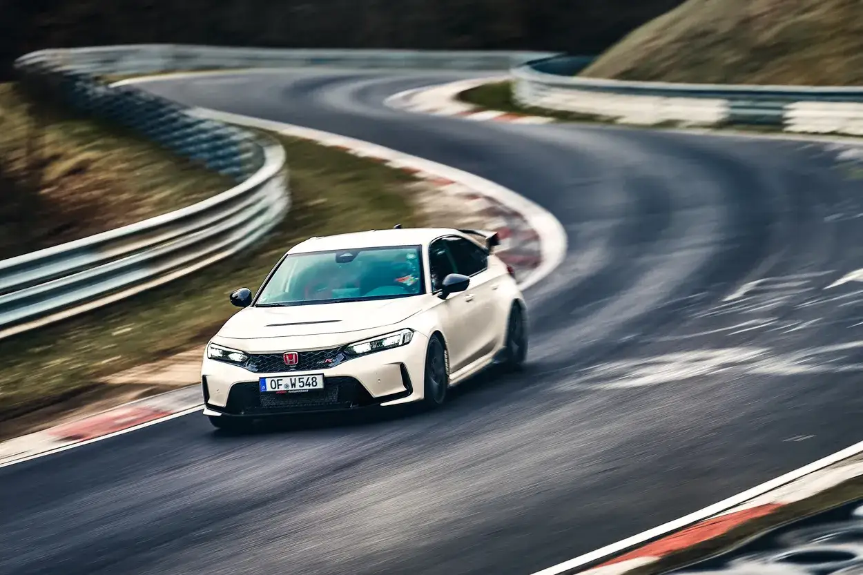Un Honda Civic Type R CV blanco acelera en una curva de un circuito, con las barreras de seguridad y el paisaje borrosos por la velocidad.