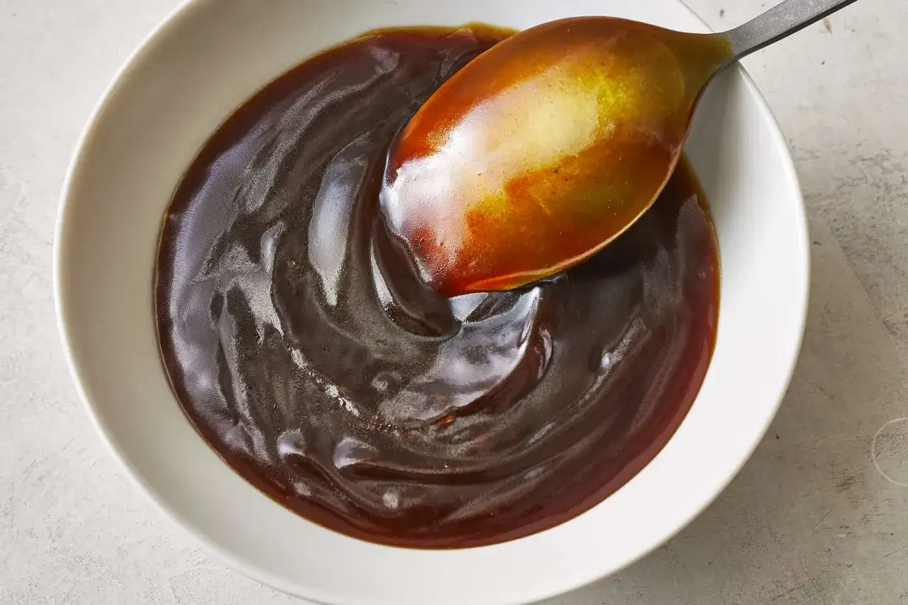 En sked lyfts ur en sk&aring;l med glansig, m&ouml;rk teriyakis&aring;s. Perfekt f&ouml;r ditt teriyakis&aring;s recept.