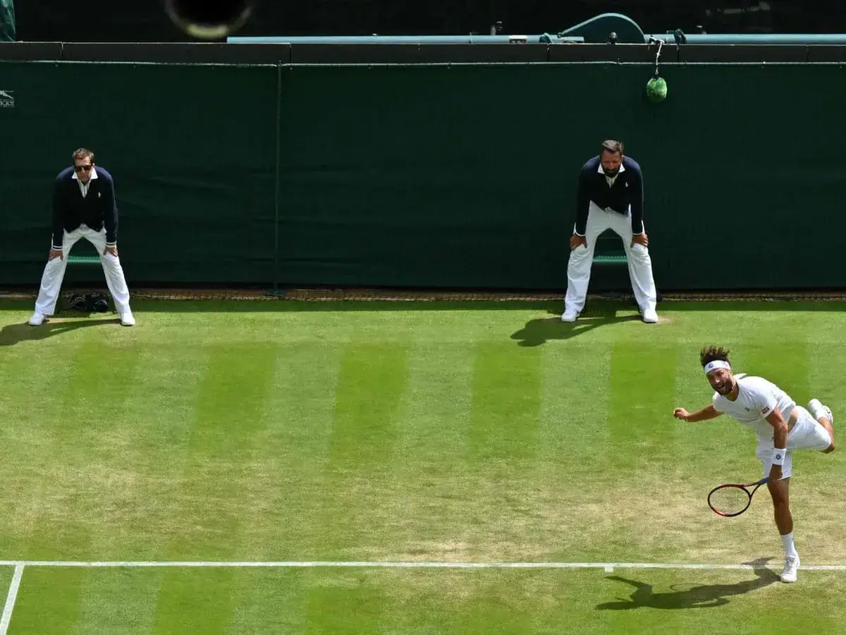 Sędziowie tenisa ziemnego WTA w białych strojach obserwują mecz na trawiastym korcie.