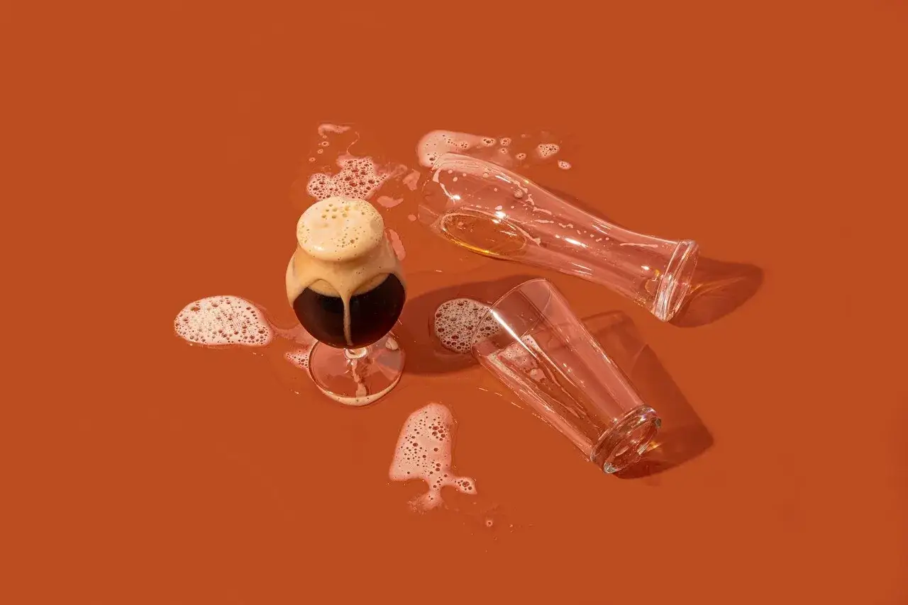 Verre de bière brune renversé, deux verres vides à côté. Une scène qui évoque une allergie à la bière.