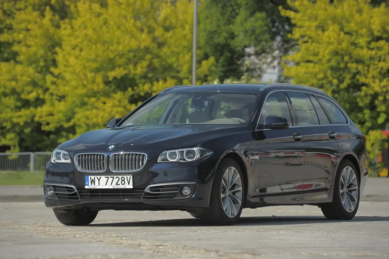 Czarne BMW 535d kombi z polskimi tablicami rejestracyjnymi stoi na tle zielonych drzew.