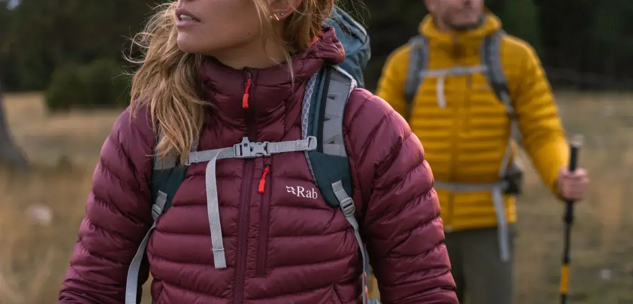 Dwie osoby w kurtkach z ociepliną **Primaloft** wędrują po szlaku. Kurtka z przodu jest bordowa, z tyłu żółta.