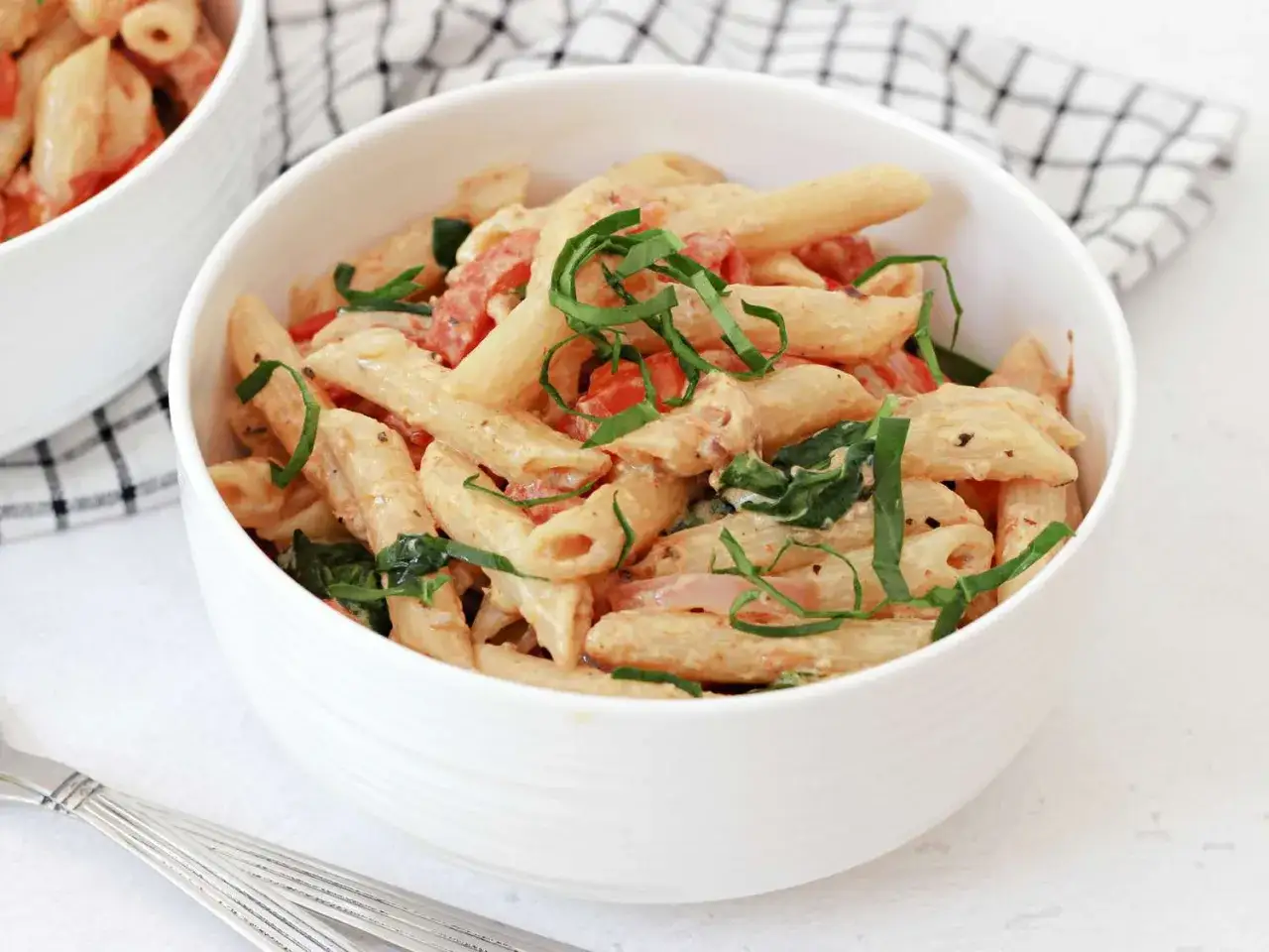 Penne z kremowym sosem, pomidorami, szpinakiem i fetą, posypane świeżą bazylią. Pyszny makaron z fetą.