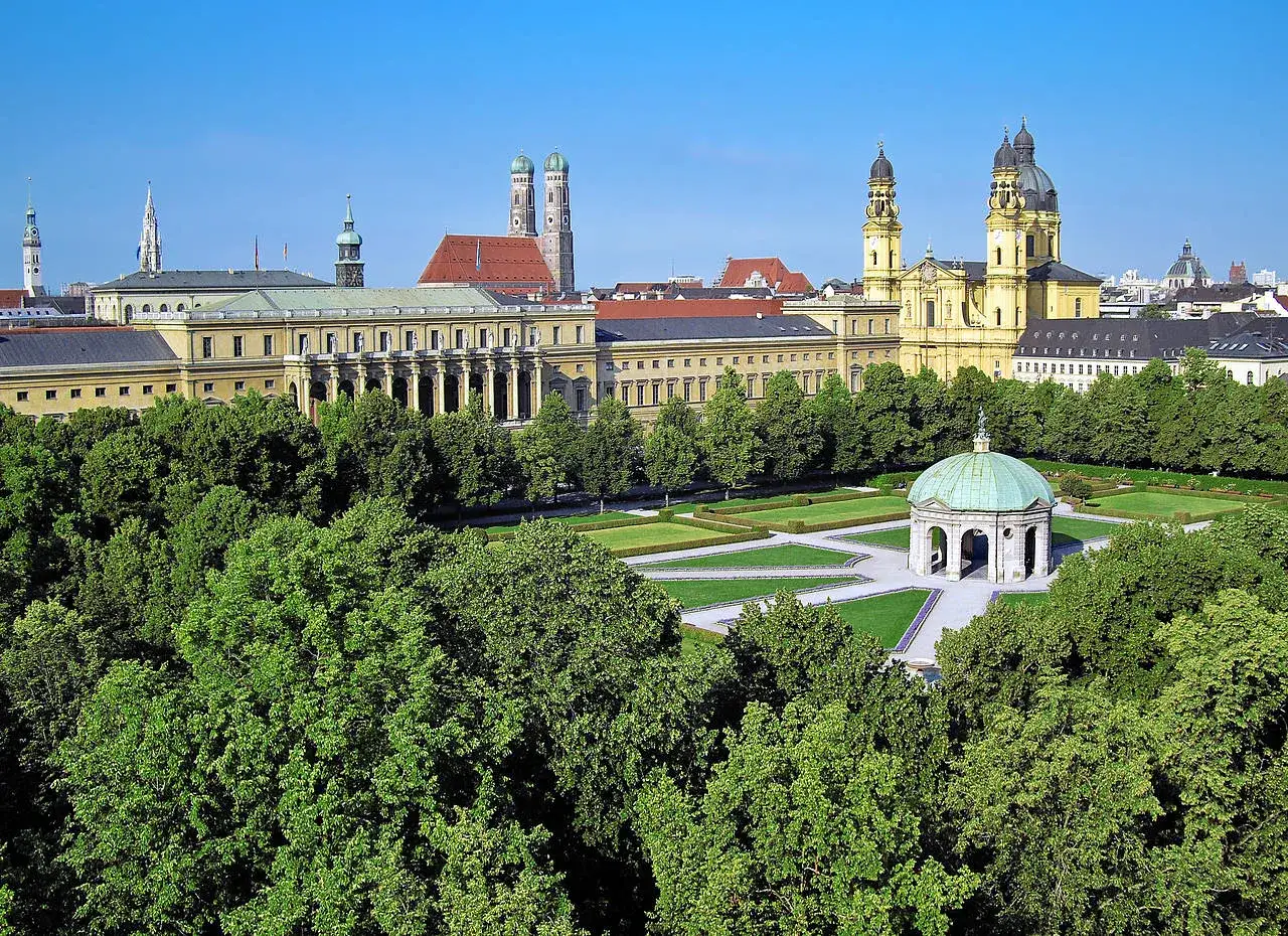 Blick über grüne Bäume auf den Odeonsplatz München mit der Theatinerkirche und dem Hofgarten.