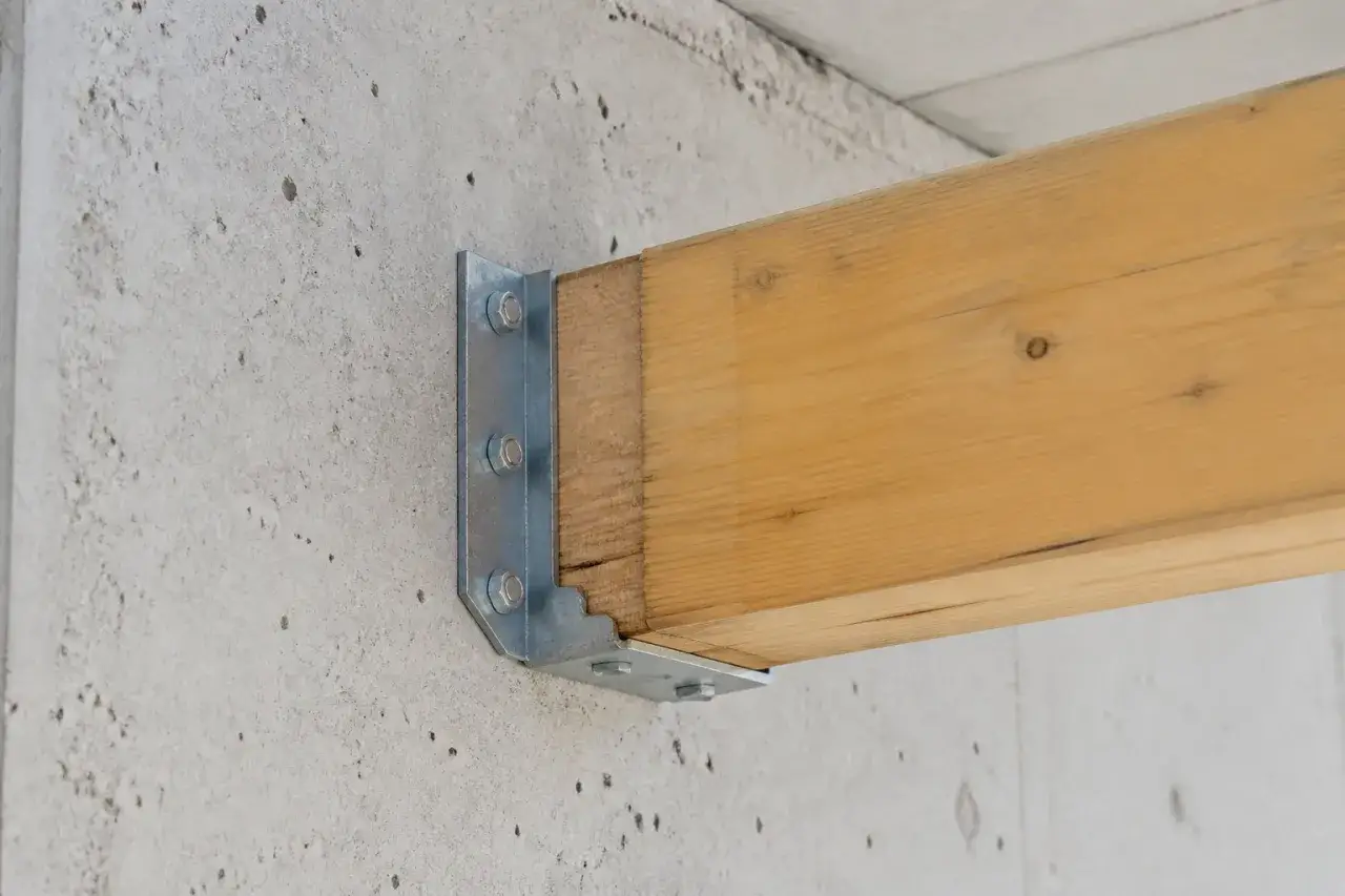 Fixation poutre bois sur mur en béton avec équerre métallique boulonnée.