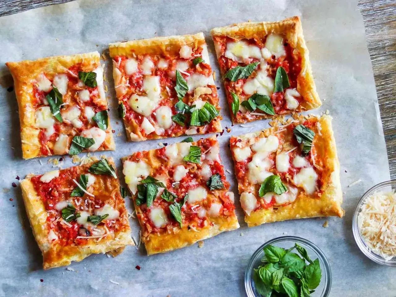 Sześć kwadratowych kawałków pysznej pizzy z ciasta francuskiego, z pomidorami, mozzarellą i bazylią.
