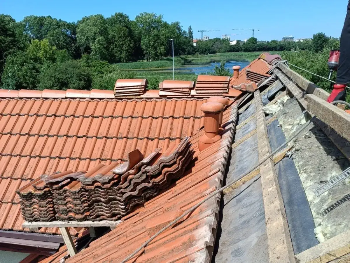 Układanie nowego dachu na starym dachu. Stare dach&oacute;wki czekają na usunięcie, a nowe są gotowe do montażu.