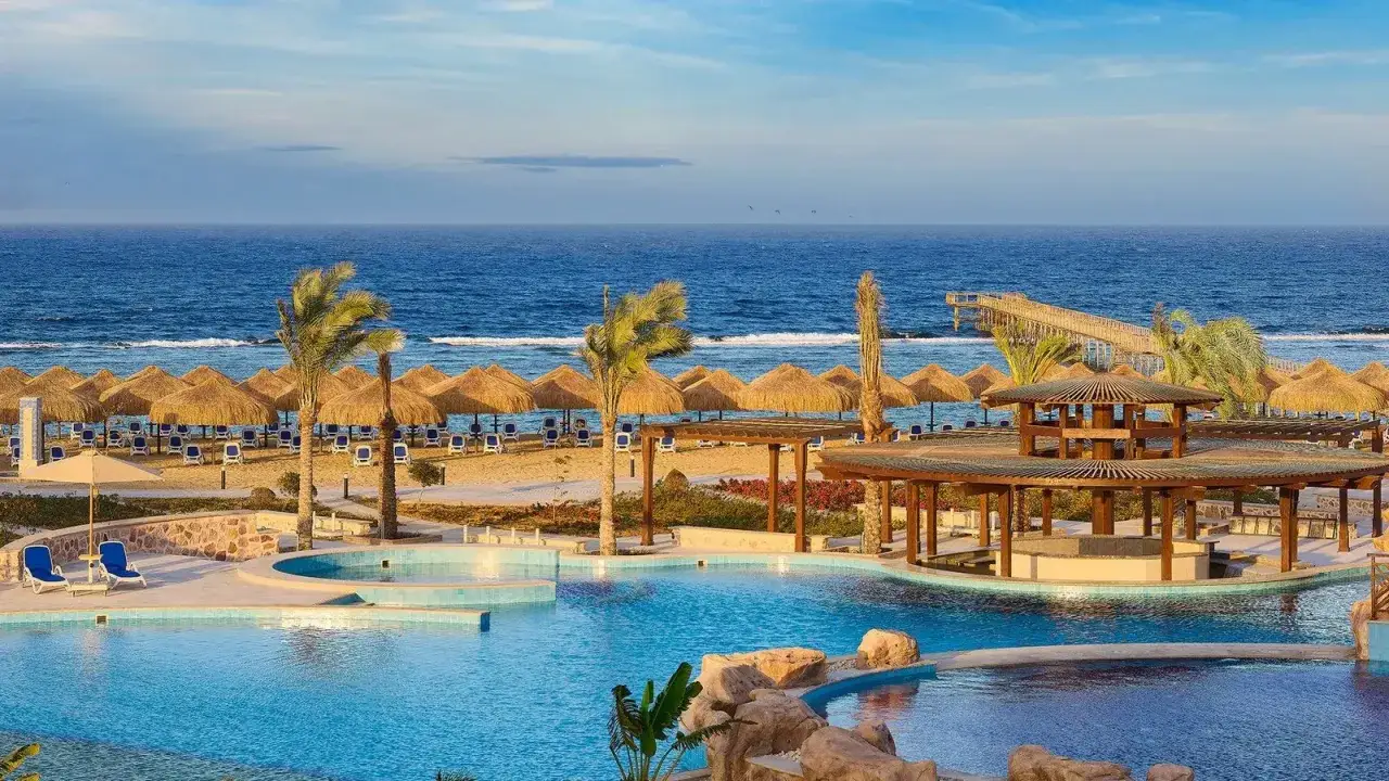 Basen i plaża z parasolami, palmami i pomostem w Pickalbatros Marsa Alam.