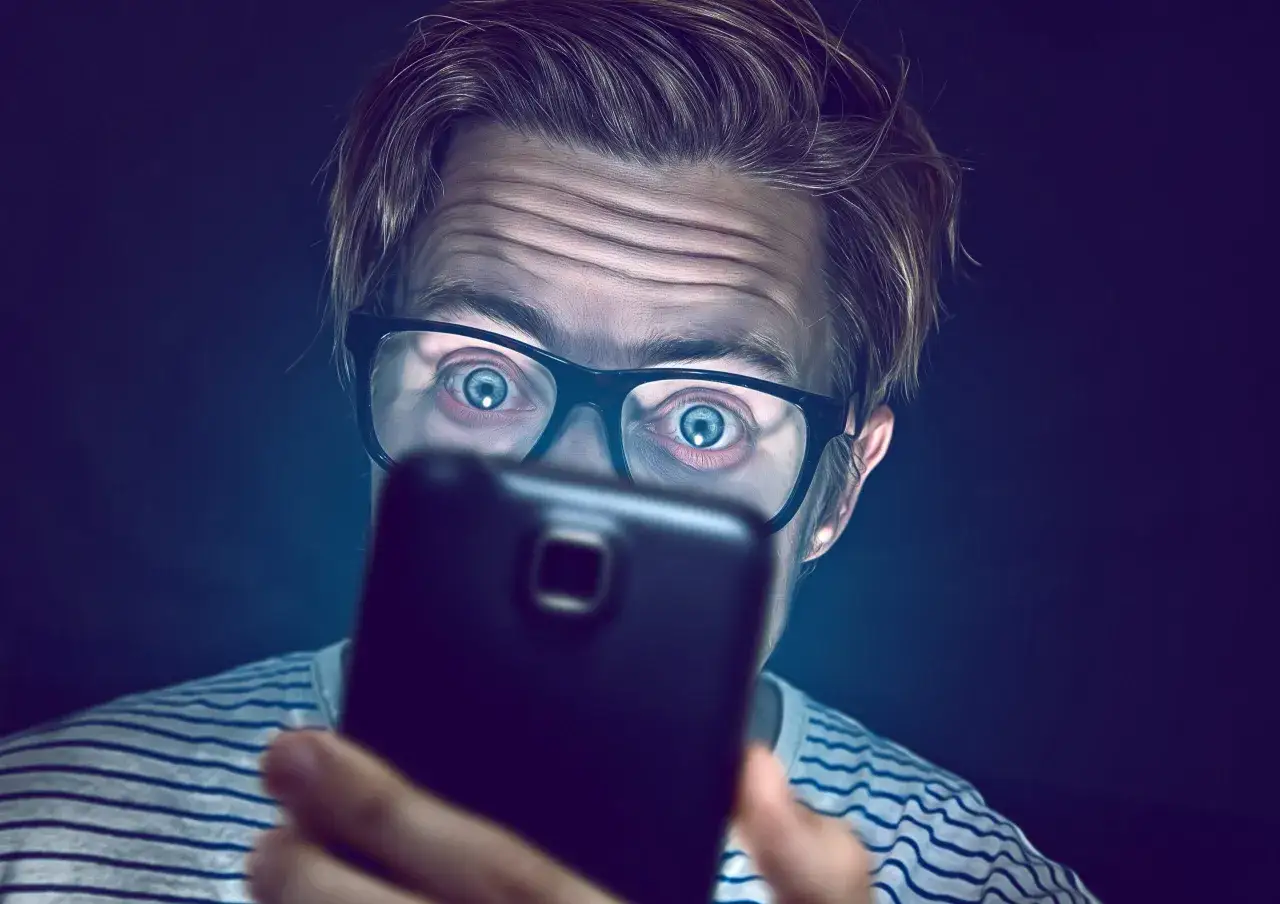 Osoba ze smartfonem, patrząca na innych ludzi, z poczuciem wykluczenia