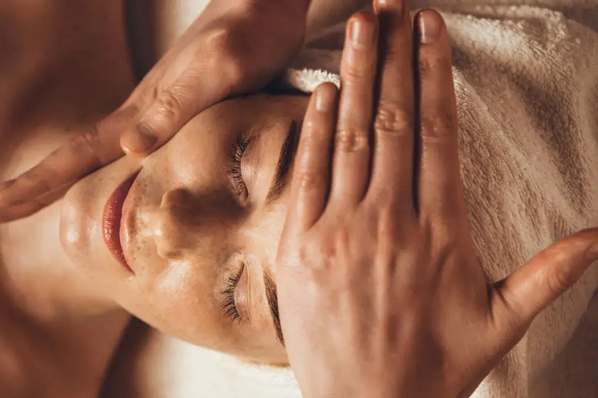A gentle hand massages a woman's face, her eyes closed in relaxation. This is a moment of pure bliss during a holistic facial treatment.