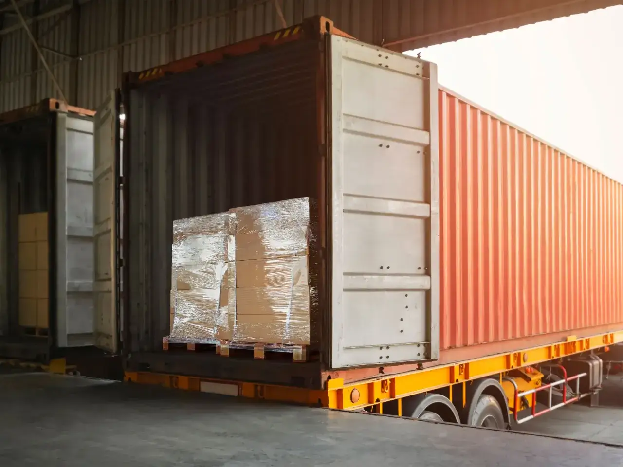 Paletten mit Waren werden in einen offenen Container geladen. Dies ist ein Beispiel f&uuml;r die Logistik von DHL Freight, die den Transport von G&uuml;tern erm&ouml;glicht.