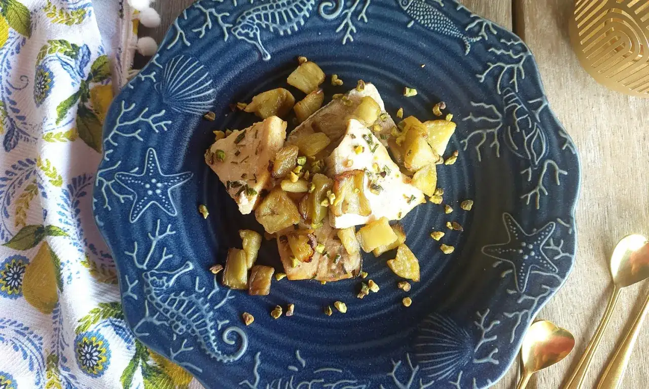 Delizioso pesce spada in friggitrice ad aria, croccante e saporito, guarnito con patate e pistacchi su un piatto a tema marino.