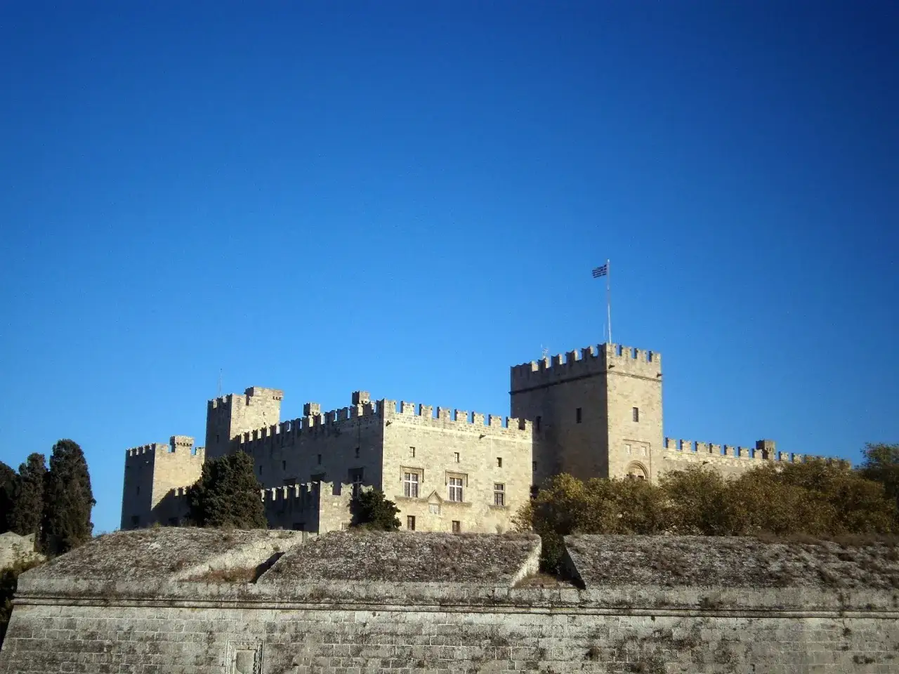 Pałac Wielkich Mistrzów w Rodos mieście, majestatyczna twierdza z grecką flagą na tle błękitnego nieba.