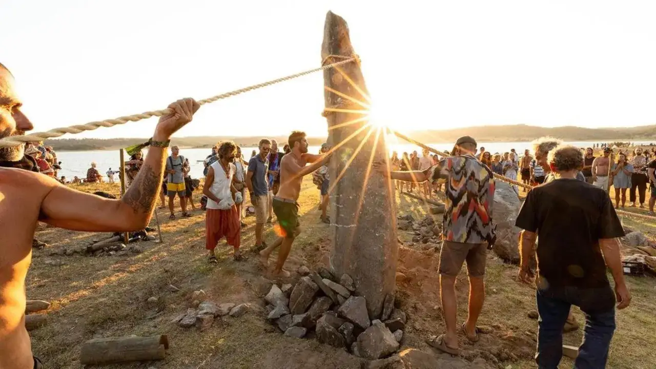 Menschen in Portugal ziehen gemeinsam ein Steinmonument auf. Die Sonne bricht durch den Stein und erzeugt einen Sterneneffekt.
