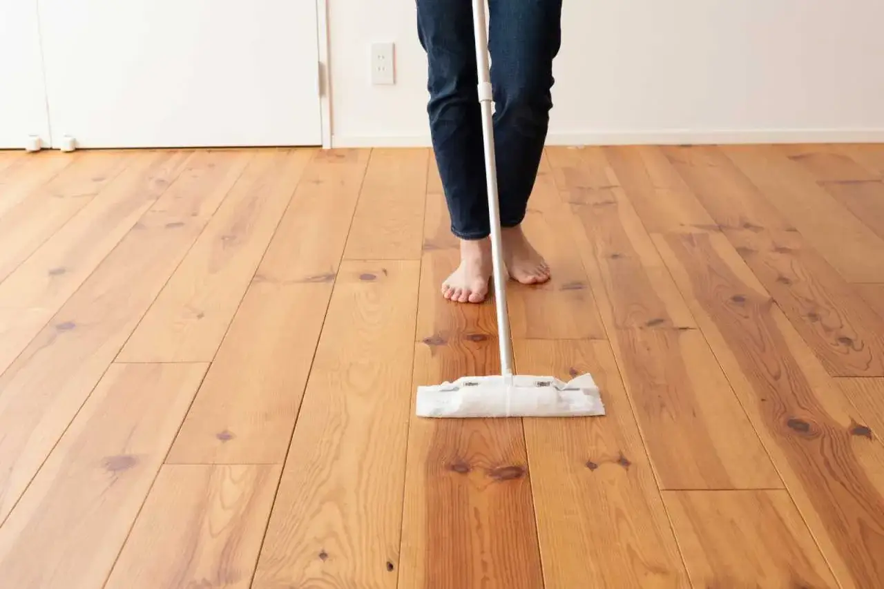 Persona descalza limpiando un suelo de madera con una mopa. Aprende como limpiar suelo de madera para mantenerlo reluciente.